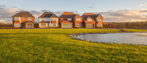 Modern red brick houses with garages, overlooking a grassy area and a small pond at sunset at Curbor