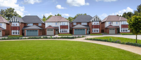 A row of modern detached houses with varied brick and render facades, set against a bright blue sky
