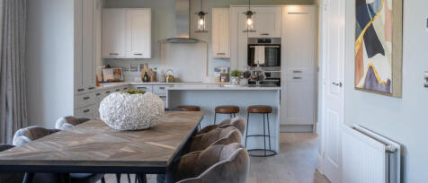 Modern open-plan kitchen and dining area with white cabinetry, a wooden dining table, and neutral de
