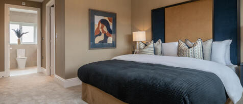 Elegant bedroom with a large bed, colourful cushions, modern art on the wall, and an en-suite bathro