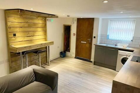 A modern one-bedroom apartment featuring an open-plan living area with a unique wooden breakfast bar, a fully fitted kitchen, a cosy bedroom with built-in storage, and a practical shower room. Bright,
