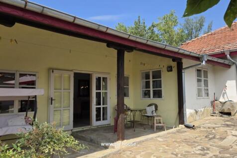 Yellow house exterior featuring white framed glass doors and windows, stone paved patio with table and chairs.