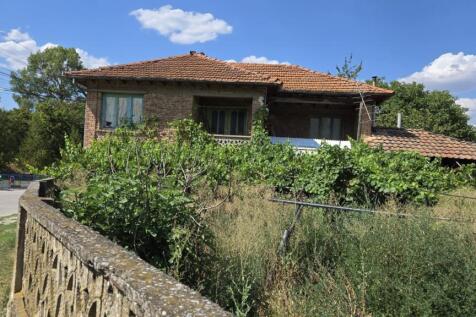 View of a two-storey brick house featuring a balcony and garden enclosed by a low wall.