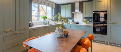 Redrow sage green kitchen design with large dining table and stylish orange chairs
