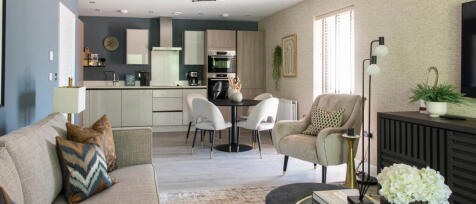 Modern open-plan living area with a kitchen, dining table, armchair, sofa, and decorative plants in